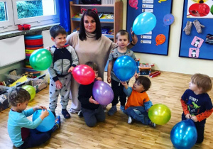 Dzieci i nauczycielka siedzą na podłodze i trzymają balony.